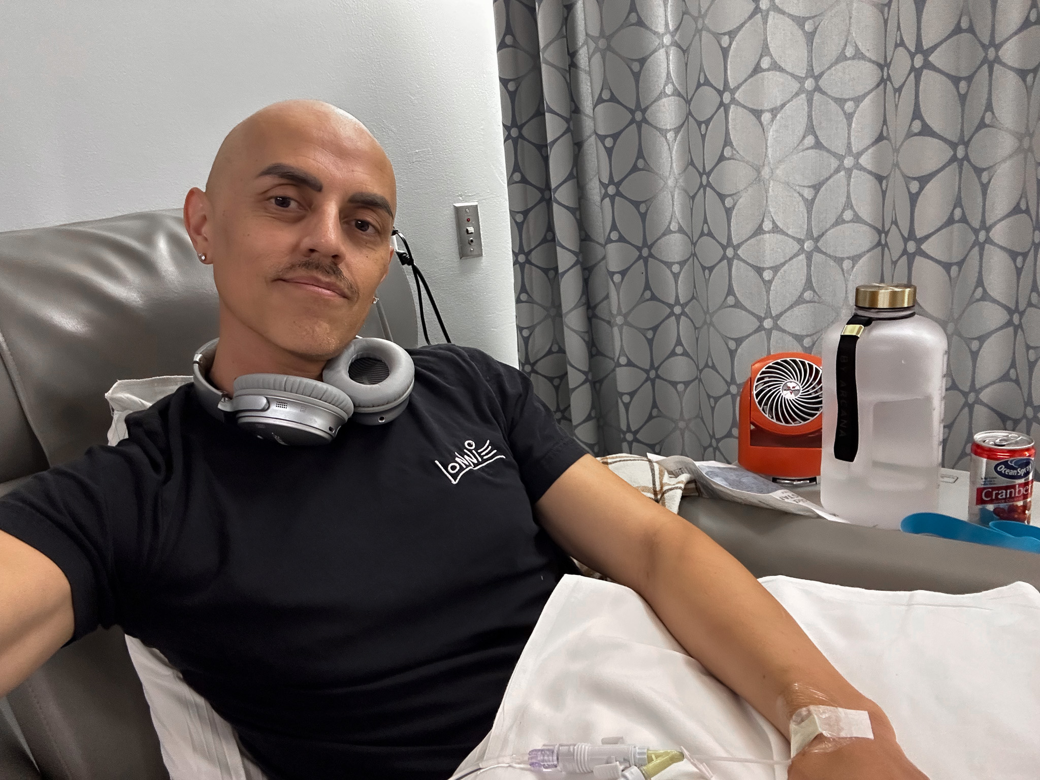 Lonnie mid-infusion, IV in his arm, wearing his own Lonnie Draws tee